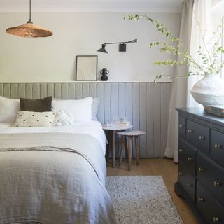 a neutral bedroom with cream coloured sheets and a black chest of drawers