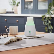 Yankee candle diffuser lit up green resting on a kitchen surface with mug, book and glasses