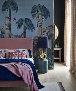 A blue bedroom with a pink bed, an exotic wall mural and a dark blue velvet bedside lamp