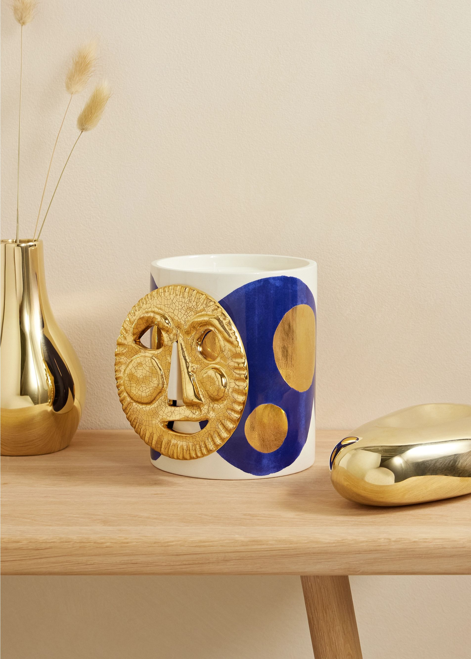 A blue and gold candle on a bench placed next to a gold base and gold piece of decor.
