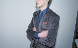 The upper portion of a male model from the nose down to the waist, his arms folded wearing a shirt and blazer