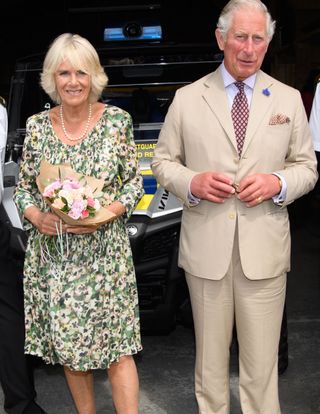 Camilla, Duchess of Cornwall, holding a bouquet of flowers and standing next to Prince Charles