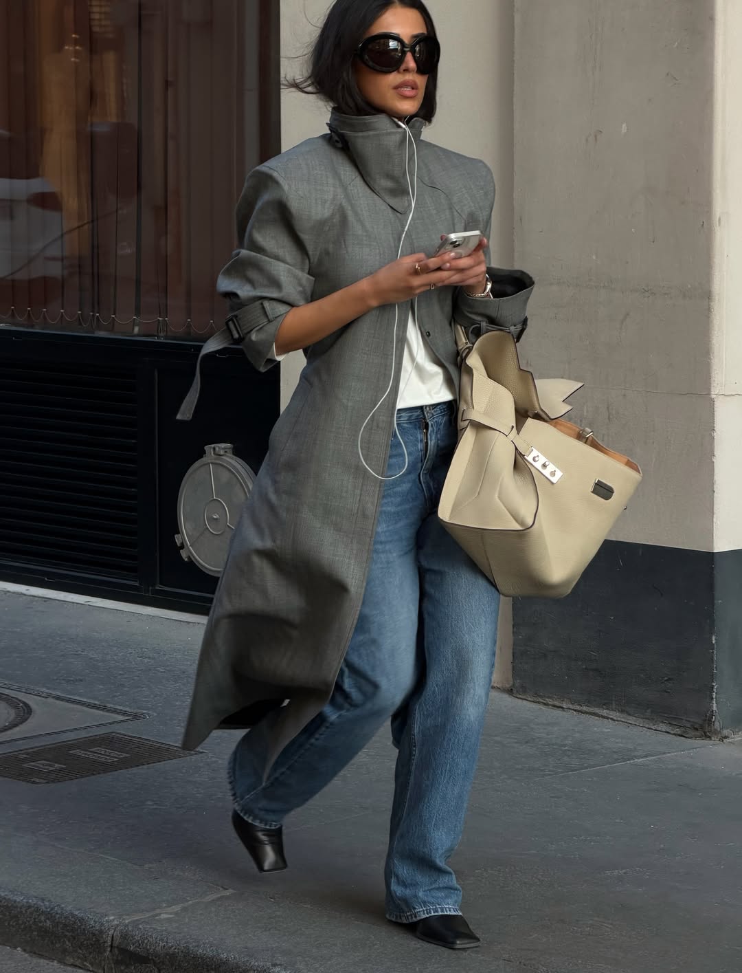 An image of @sherienboni wearing a grey trench coat with blue jeans.