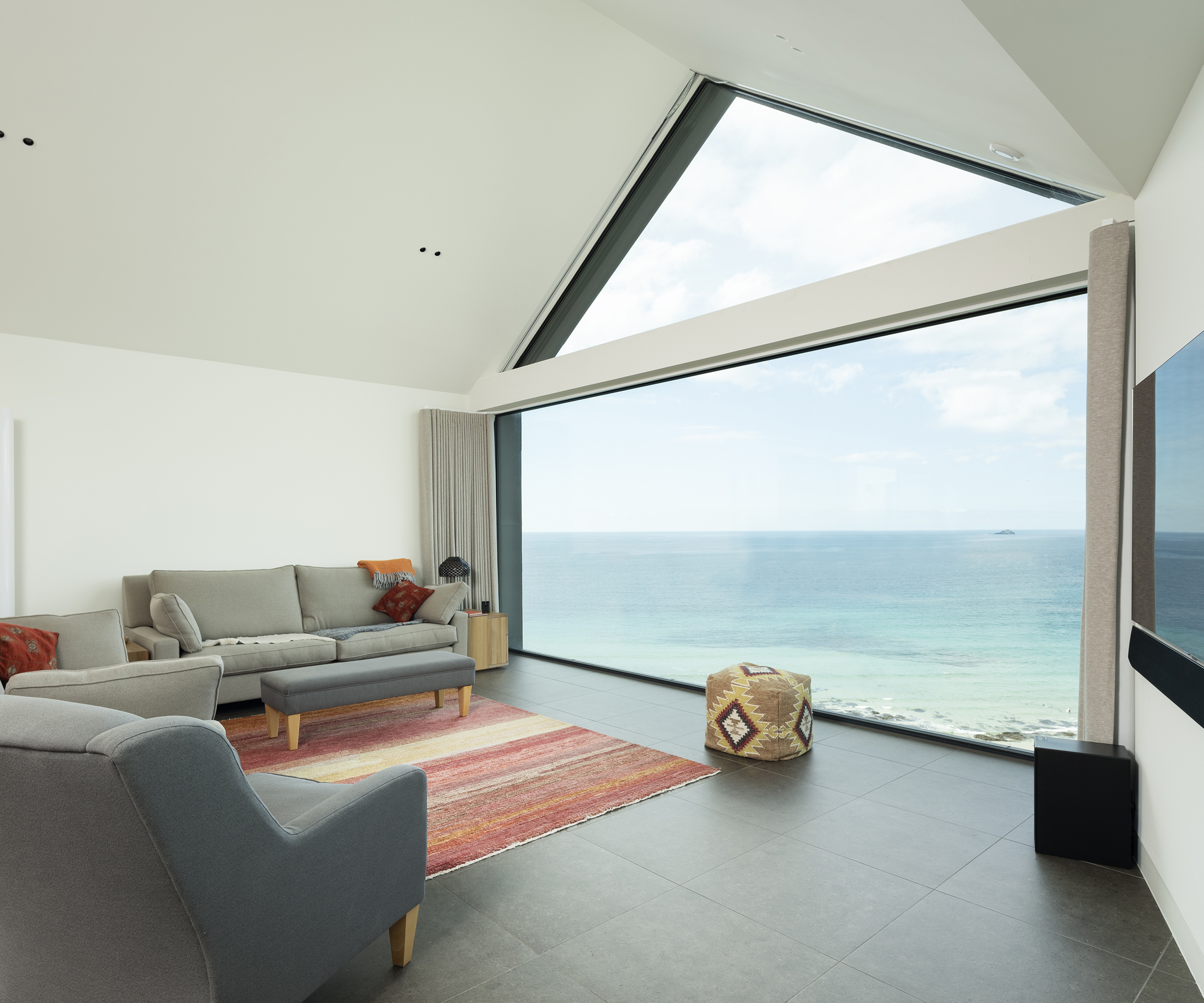 A large living room area in a contemporary self build home. There is a large picture window along a whole stretch of wall with views out to sea