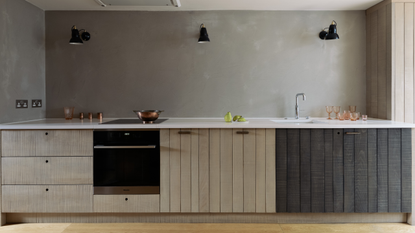 A onee wall kitchen of floor cabinets only in two tones of panelled wood and three evenly positioned wall lights across the back wall