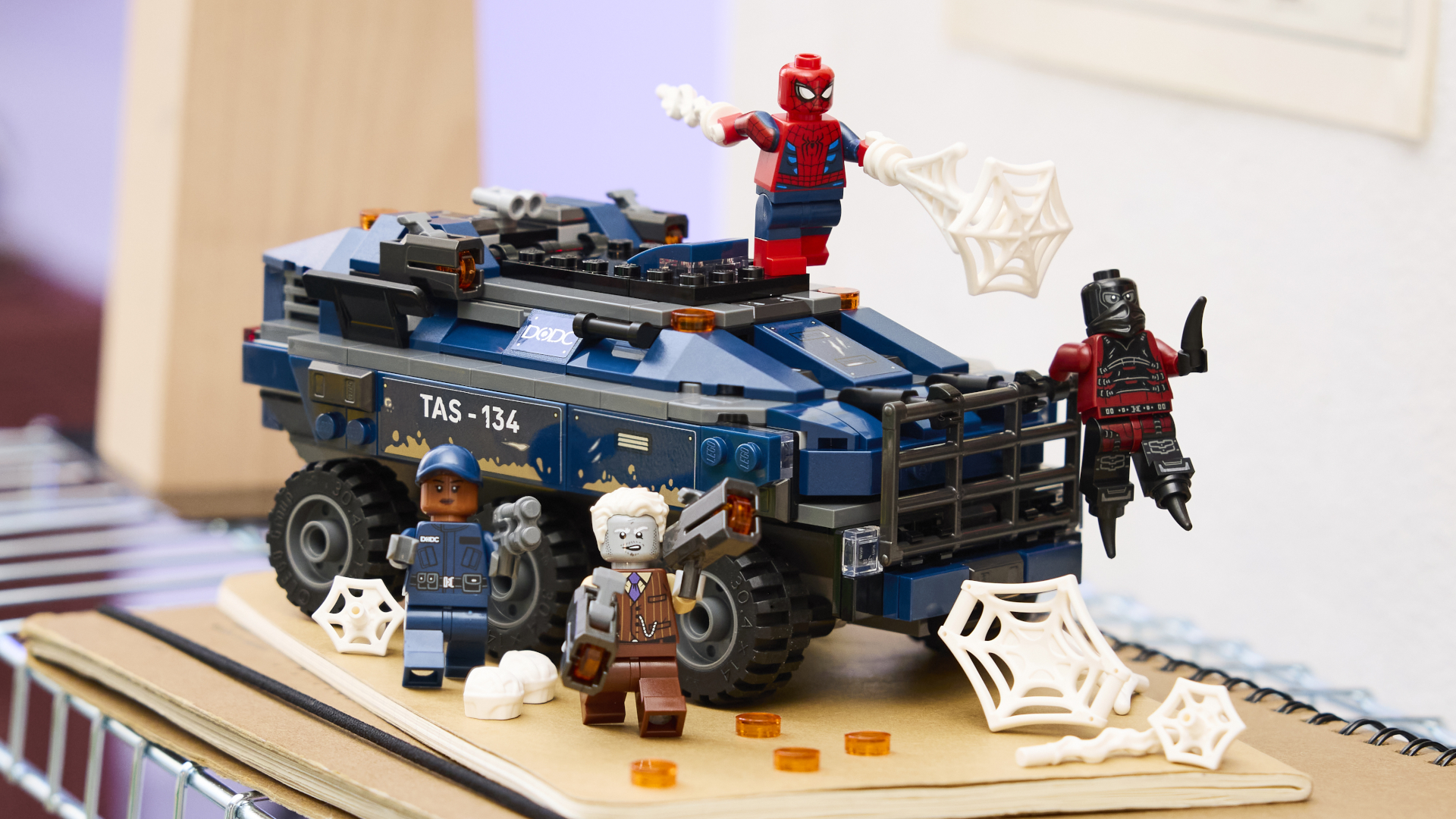 Lego Spider-Man, Tombstone, Tarantula, and guard minifigures on a prison armored vehicle, all laid out on a book