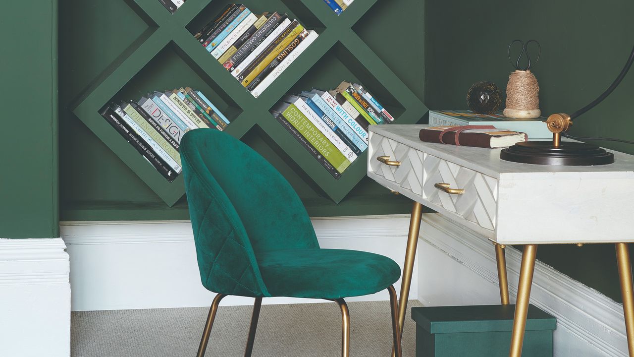 A green-painted home office with shelving, a desk and a velvet chair