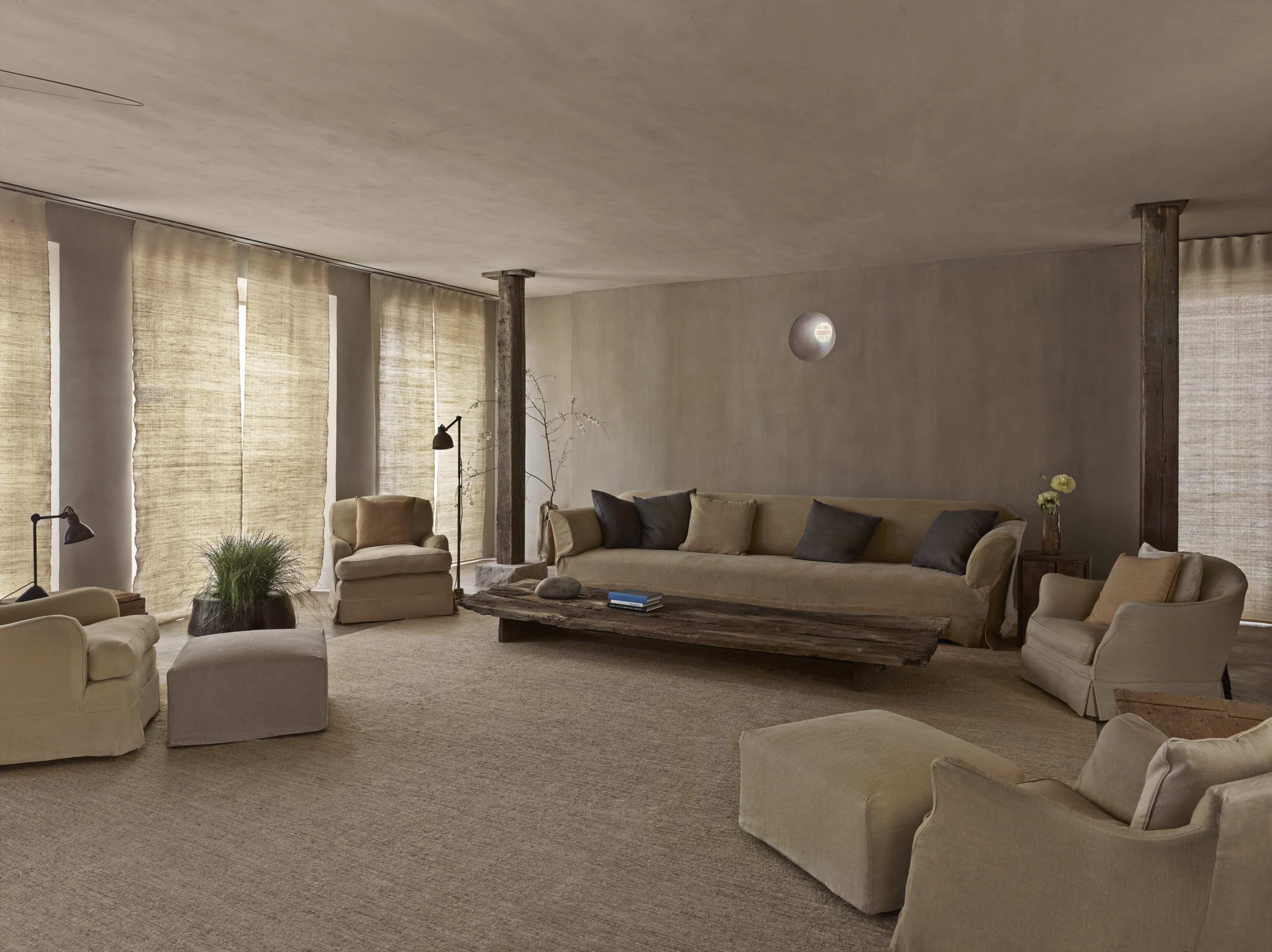 a rustic, minimalist hotel suite designed by axel vervoordt with a number of linen seats in a limewash style room