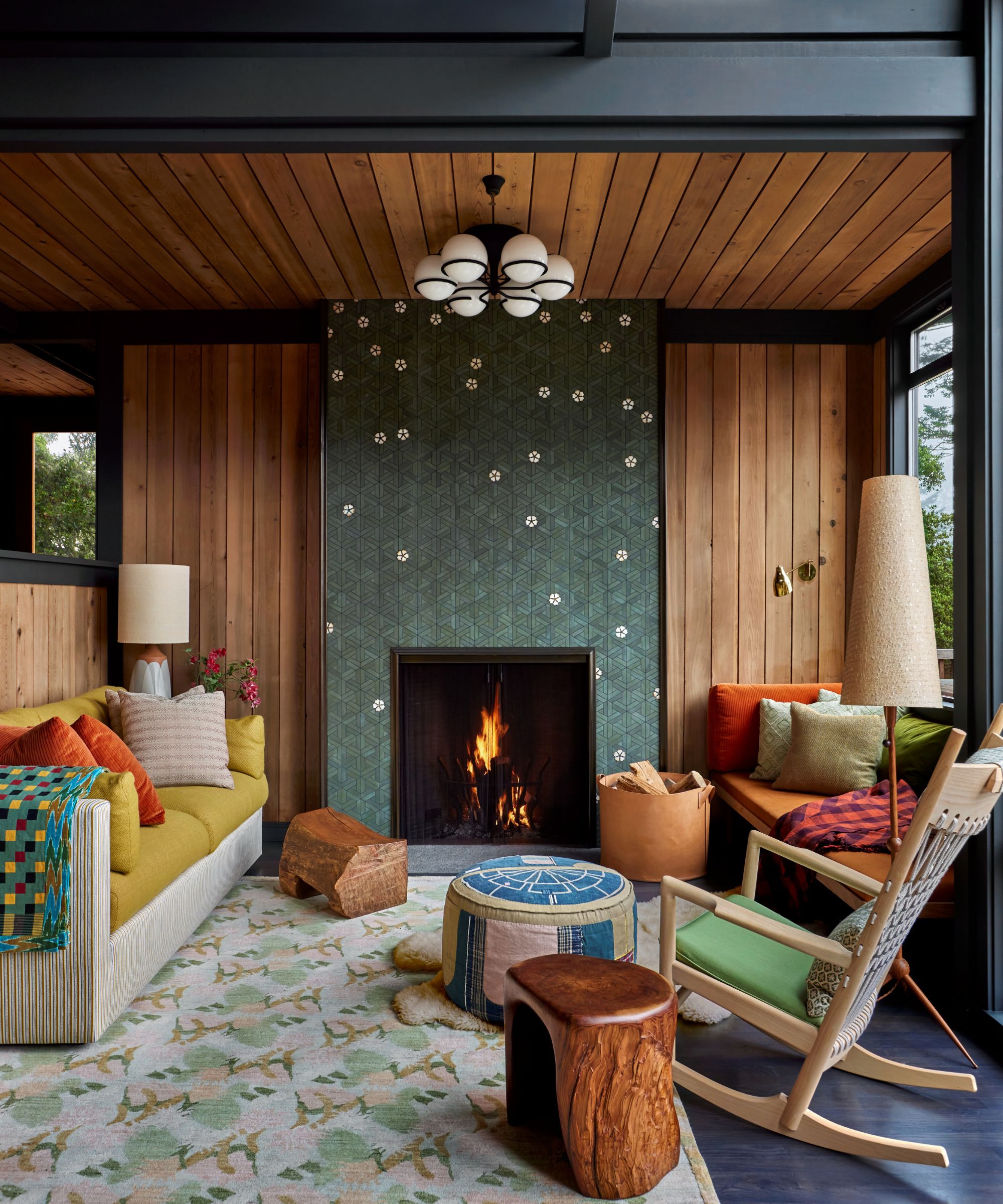 Living room with wood panelled wall and ceiling, tiled fireplace, large rug, and yellow sofa and rocking chair