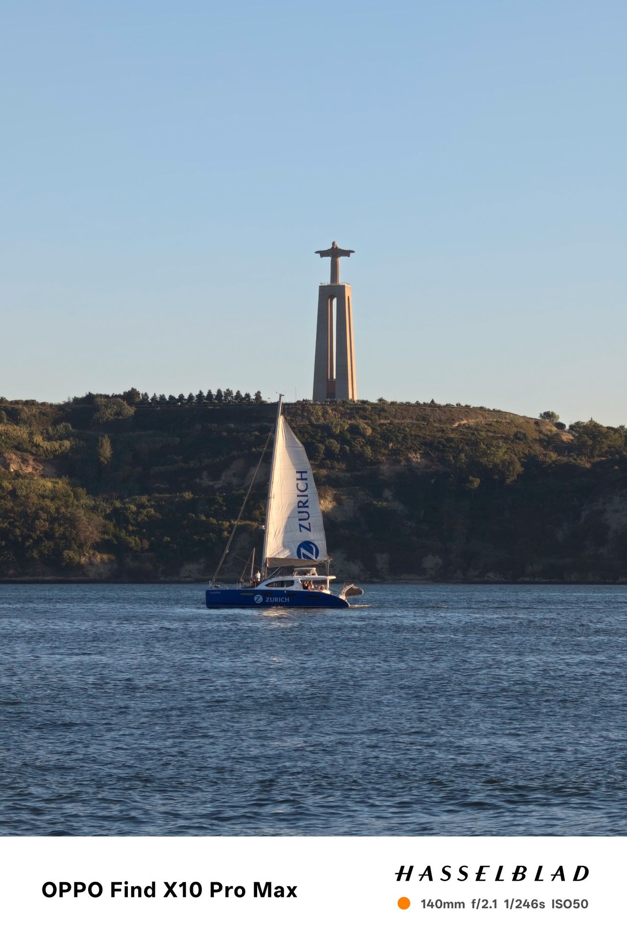 Sailboat crossing the Tagus River with the Cristo Rei monument on the hillside behind.