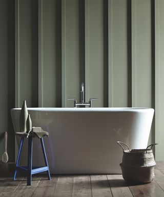 sage green bathroom wall, painted panelling, white tub, blue stool, wooden floor boards