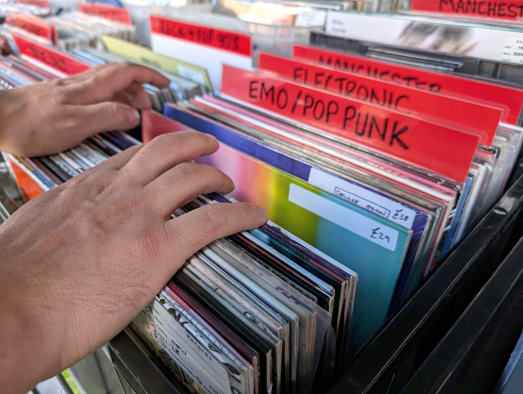 A man's hands are shown going through vinyl records at a store. The section is in front of Emo/Pop Funk.