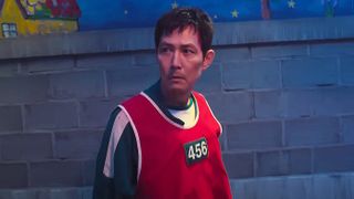 Seong G-hun wearing his green jumpsuit and a red bib with 456 on it in Squid Game season 3