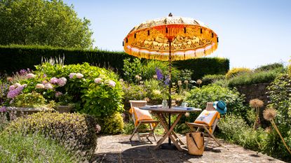 Roost episode 2 - patio with fringe parasol and outdoor furniture in large garden - Pic-credit-East-London-Parasol-Company