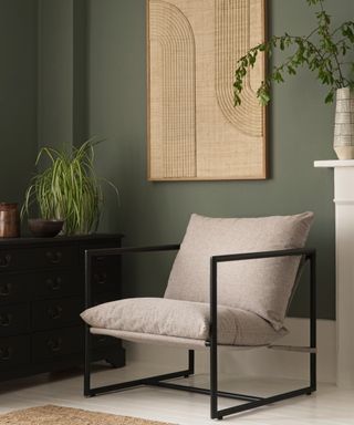 beige padded armchair with simple metal frame against green wall