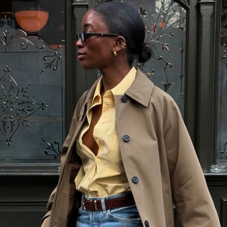 @_livmadeline wearing the cropped trench coat trend, a yellow button-down, blue jeans, slingback flats, and brown belt