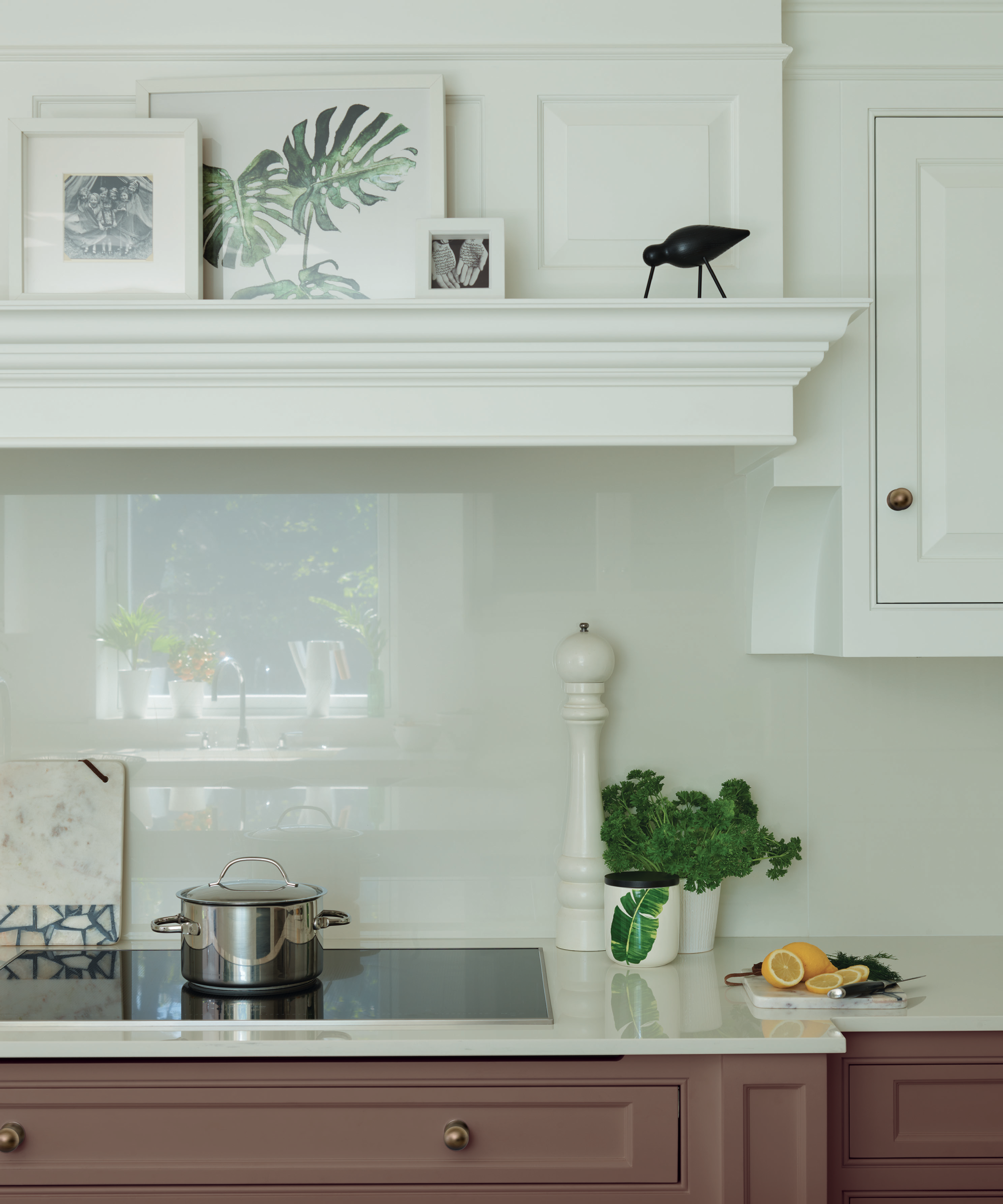A kitchen with white and dark pink cabinets with an induction hob in front of a reflective backsplash
