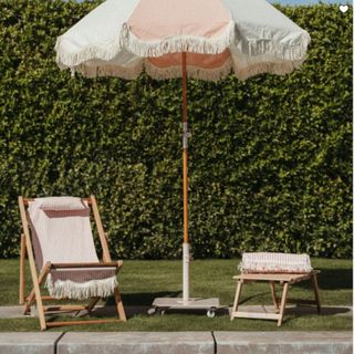 A pink and white standing outdoor umbrella with fringe at the edges from West Elm