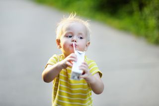 A toddler drinks juice from a juice box