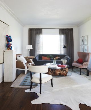 A living room with grey curtains, navy blue sofa, brown leather and velvet armchairs, wall artwork and a sculpture on a plinth armchir