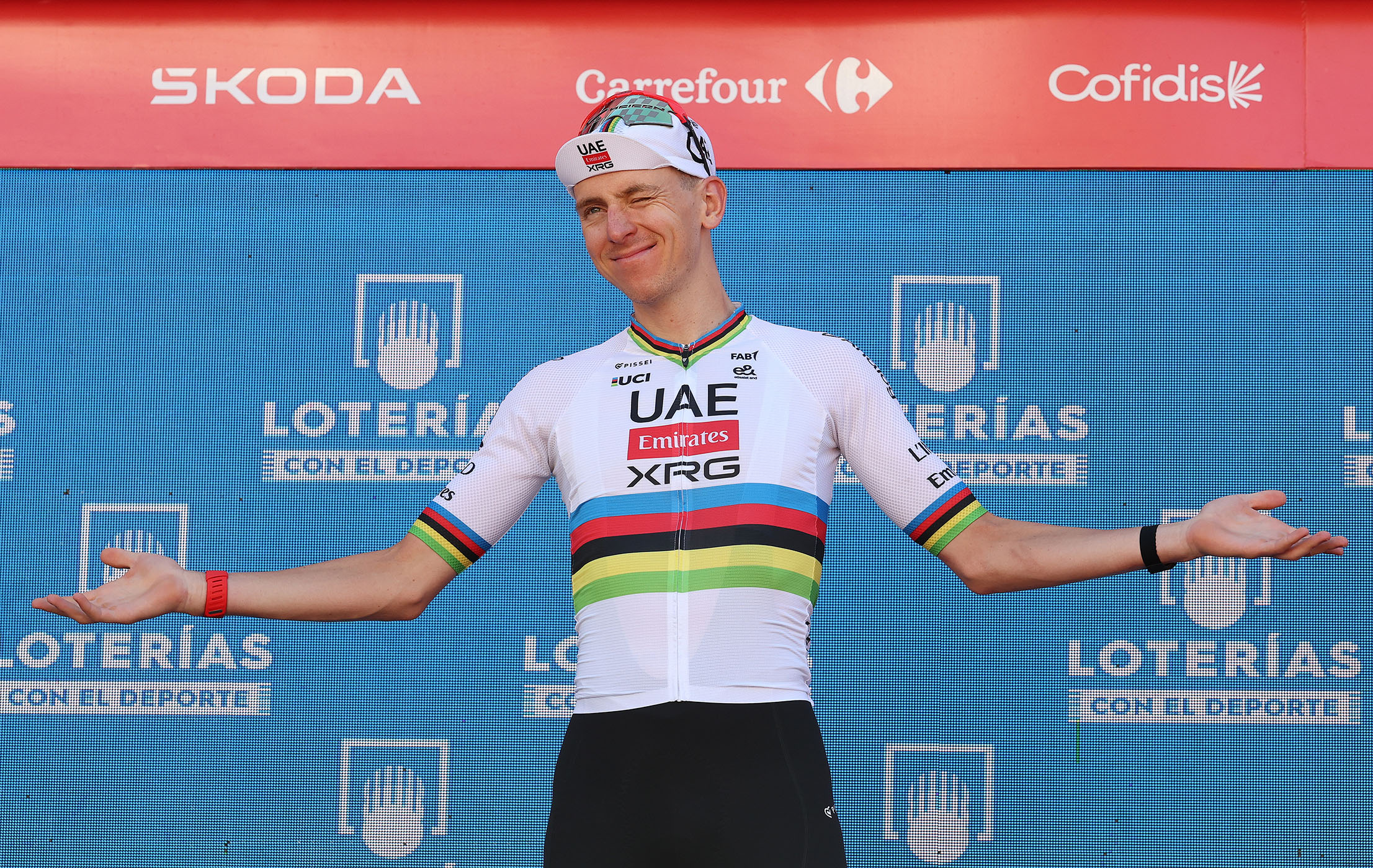 Tadej Pogacar with the rainbow jersey holds his arms out on the podium