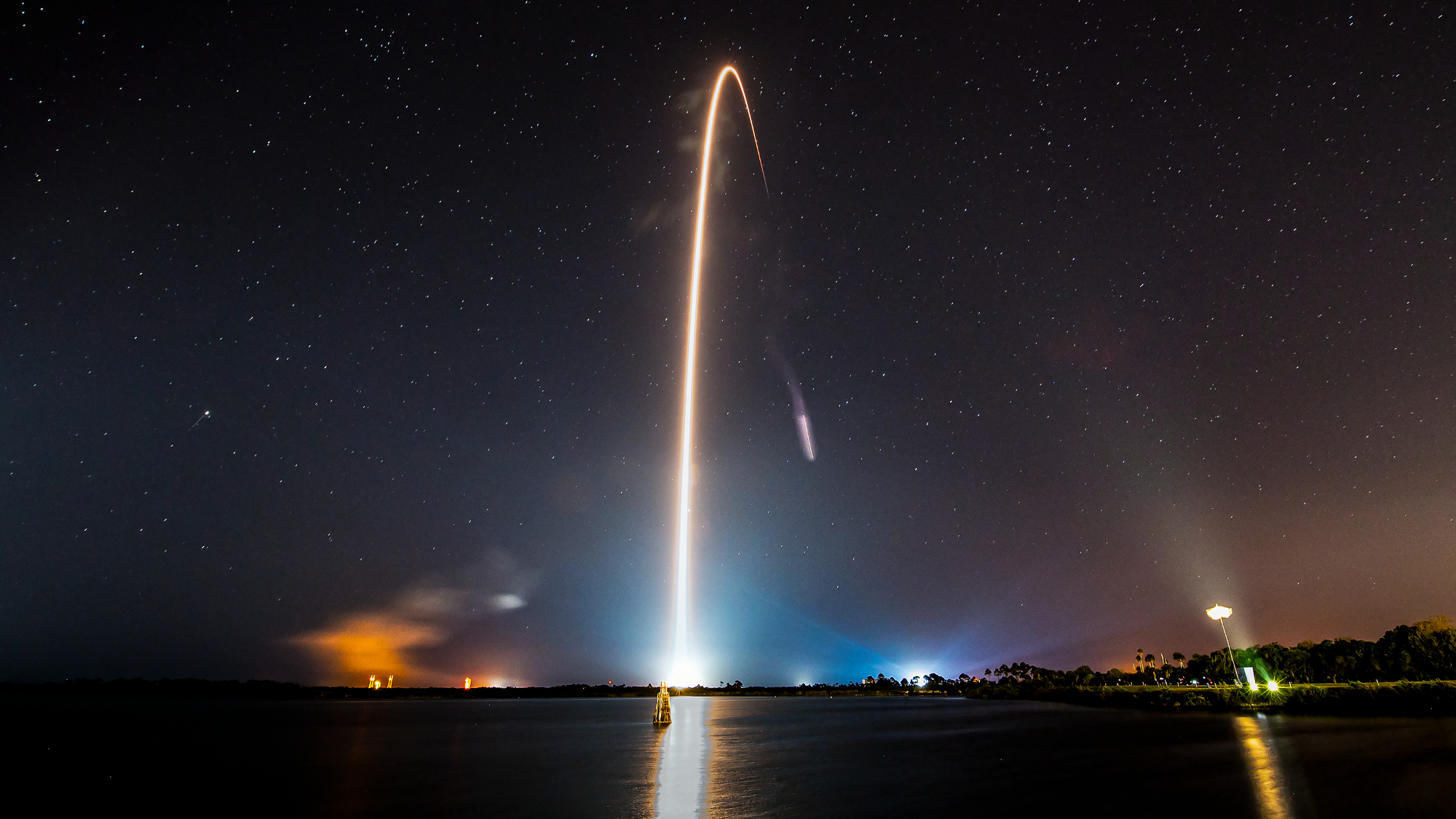 A launch rocket carves a yellow-orange arc across a dark sky