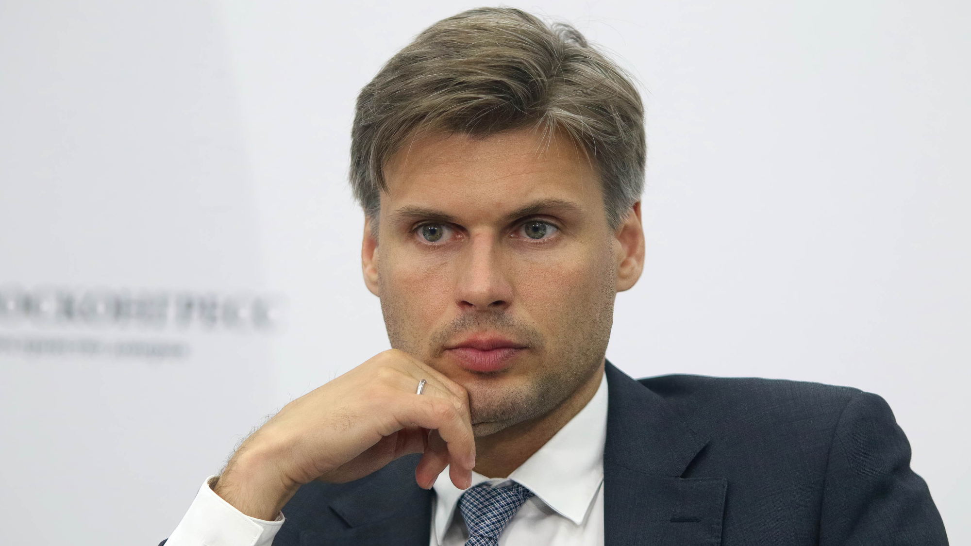 a handsome man in a dark suit gazes beguilingly into the middle distance while resting his chiseled chin on his hand