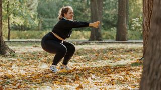 Woman doing a bodyweight squat among leaves in a park