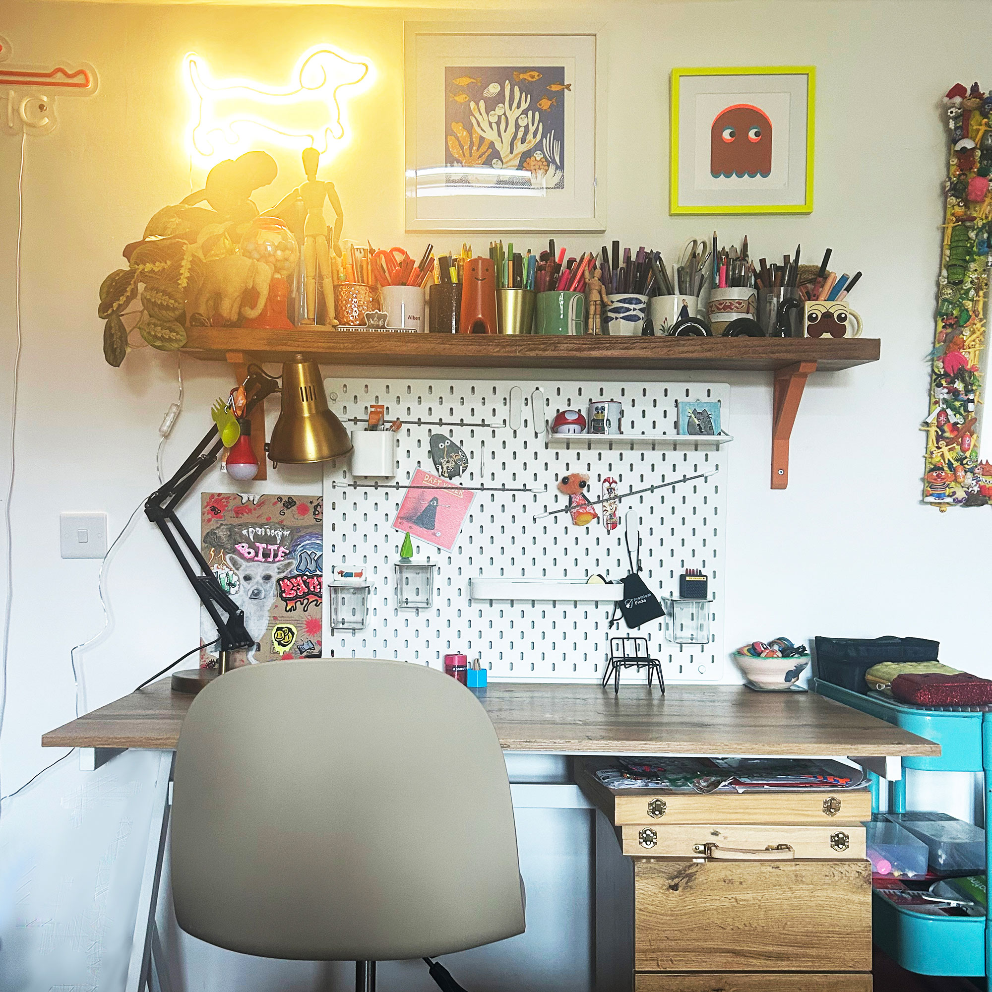 Teenage boy bedroom desk topped with open shelf filled with pens and pencils, below with framed artwork and neon light