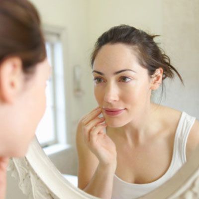 woman looking at her skin in the mirror