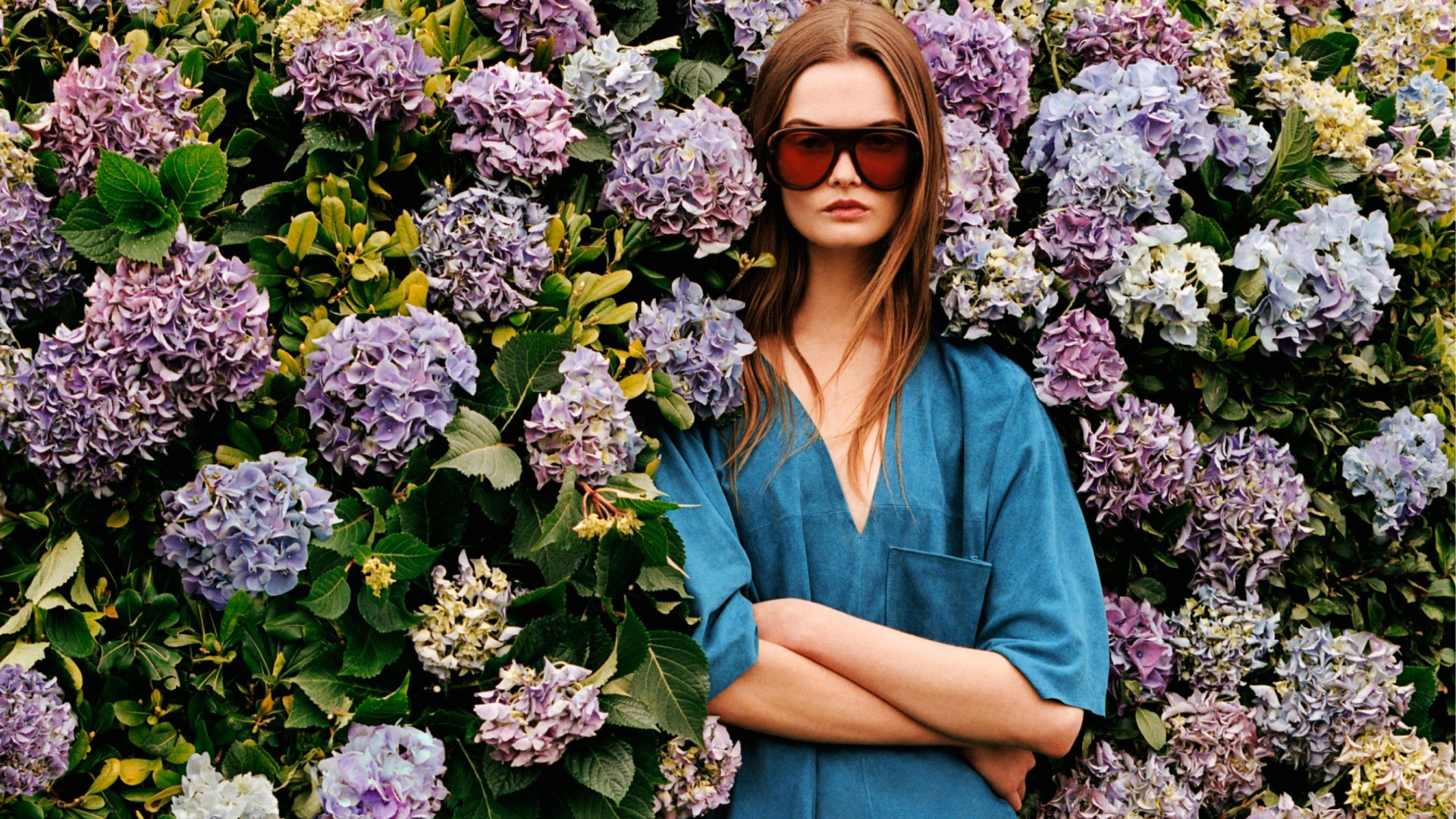 A zara model wearing the Limited Edition Suede Kaftan Dress and sunglasses standing in front of flowers 