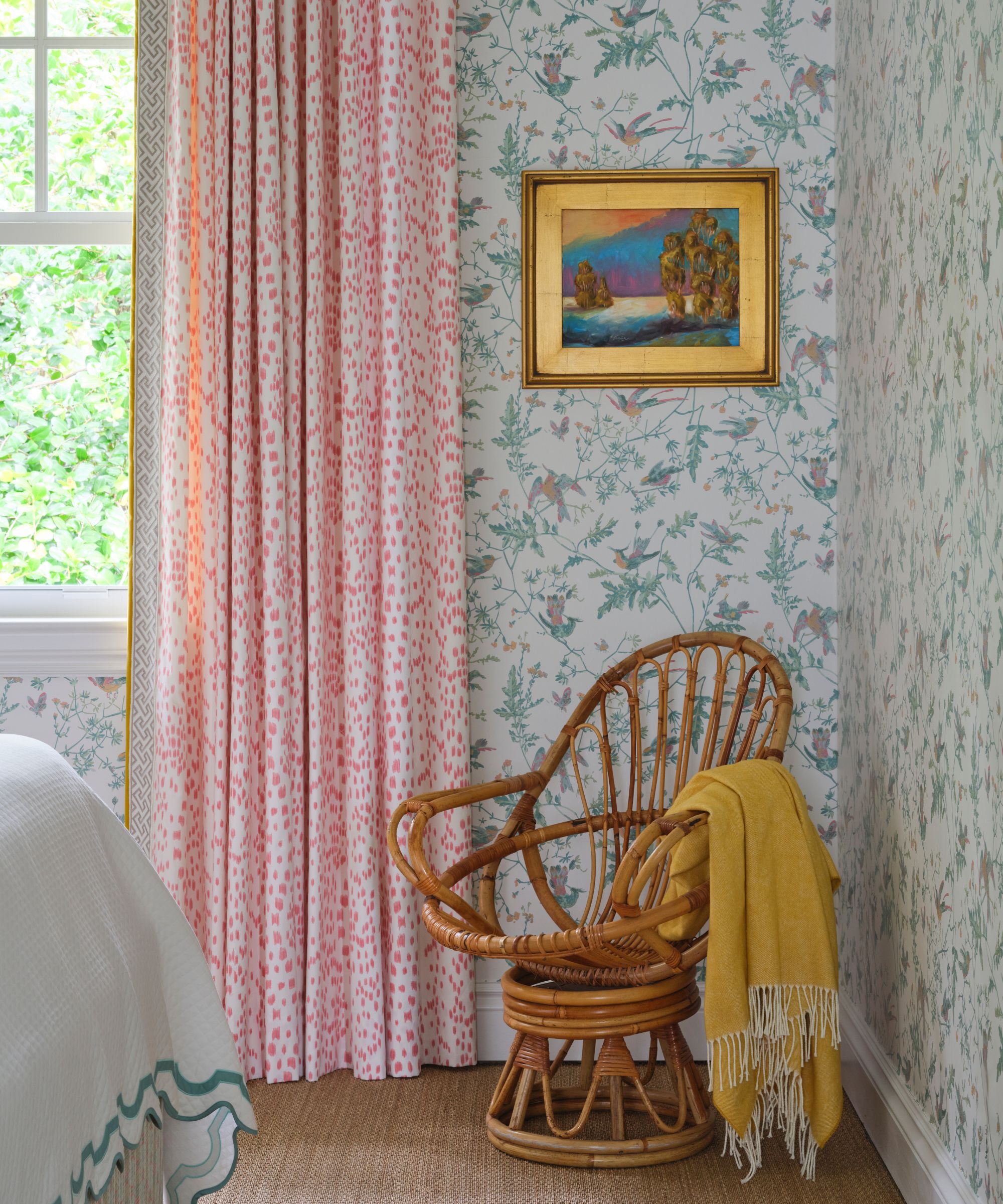 Bedroom with wallpaper on walls, polka dot curtains, rattan swivel chair and yellow throw
