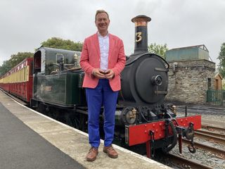 Michael Portillo stands on a station platform in front of a steam locomotive