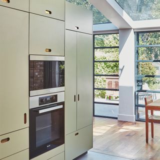 Sage green kitchen cabinetry with built-in-oven appliance and skylight on ceiling