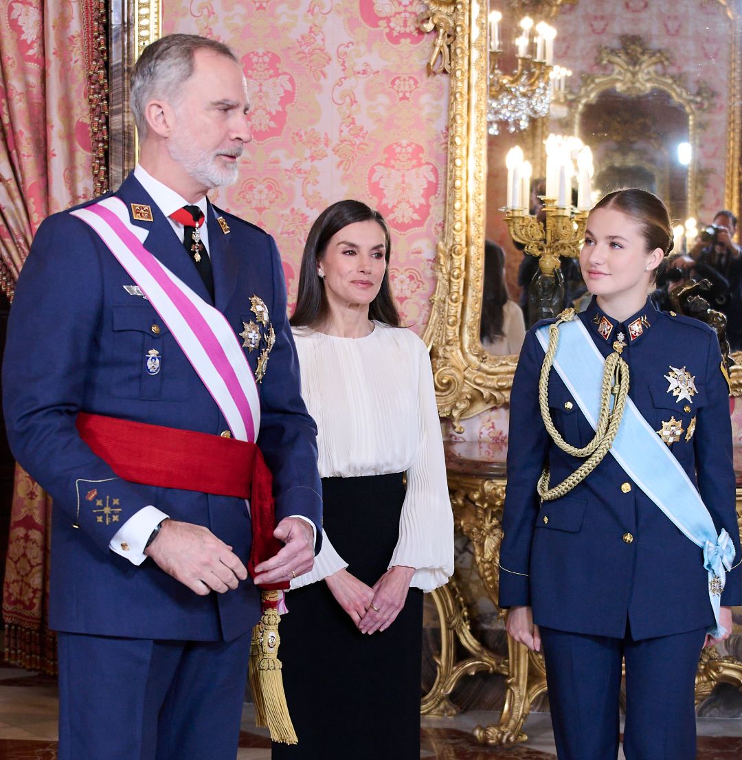 King Felipe and Princess Leonor wearing military uniforms standing with Queen Letizia in a white top and black pants