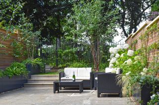Patio space with dark outdoor furniture, white cushions, subtle surrounding planting