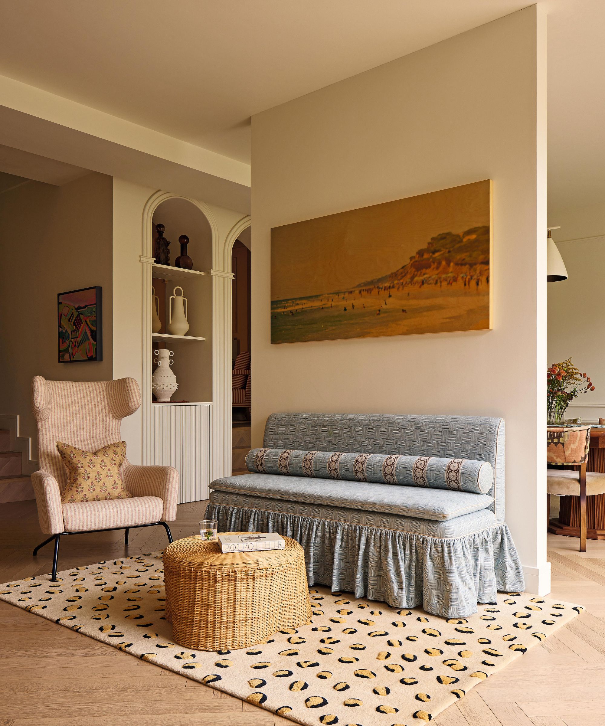 a neutral kitchen diner with a small settee area with skirted design detail, sat on a leopard print rug with a wicker coffee table