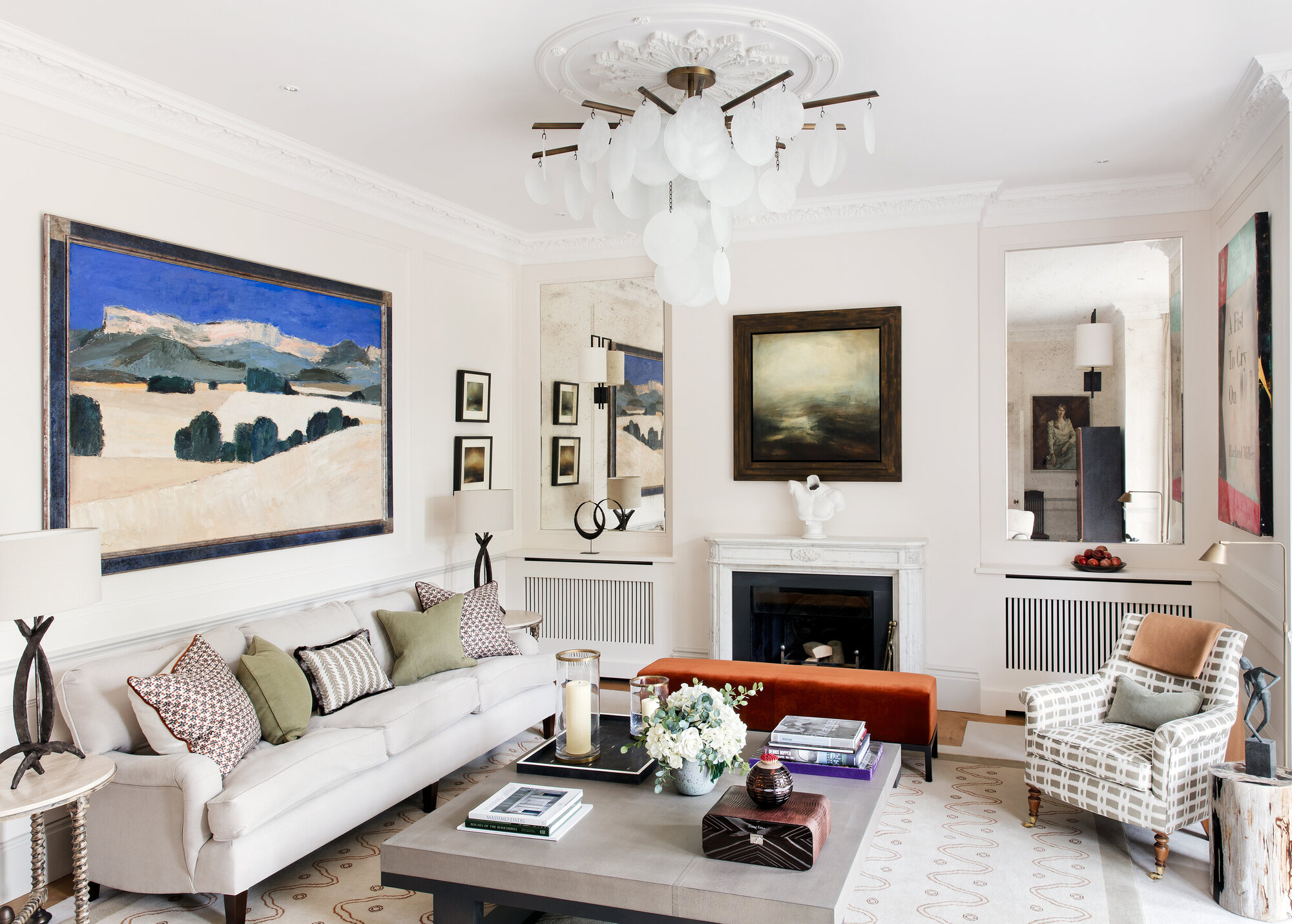 modern living room with beige sofa styled with cushions, fireplace, square coffee table styled with books, a patterned armchair, an artwork hung on the wall above the sofa and a pendant light suspended from a ceiling rose