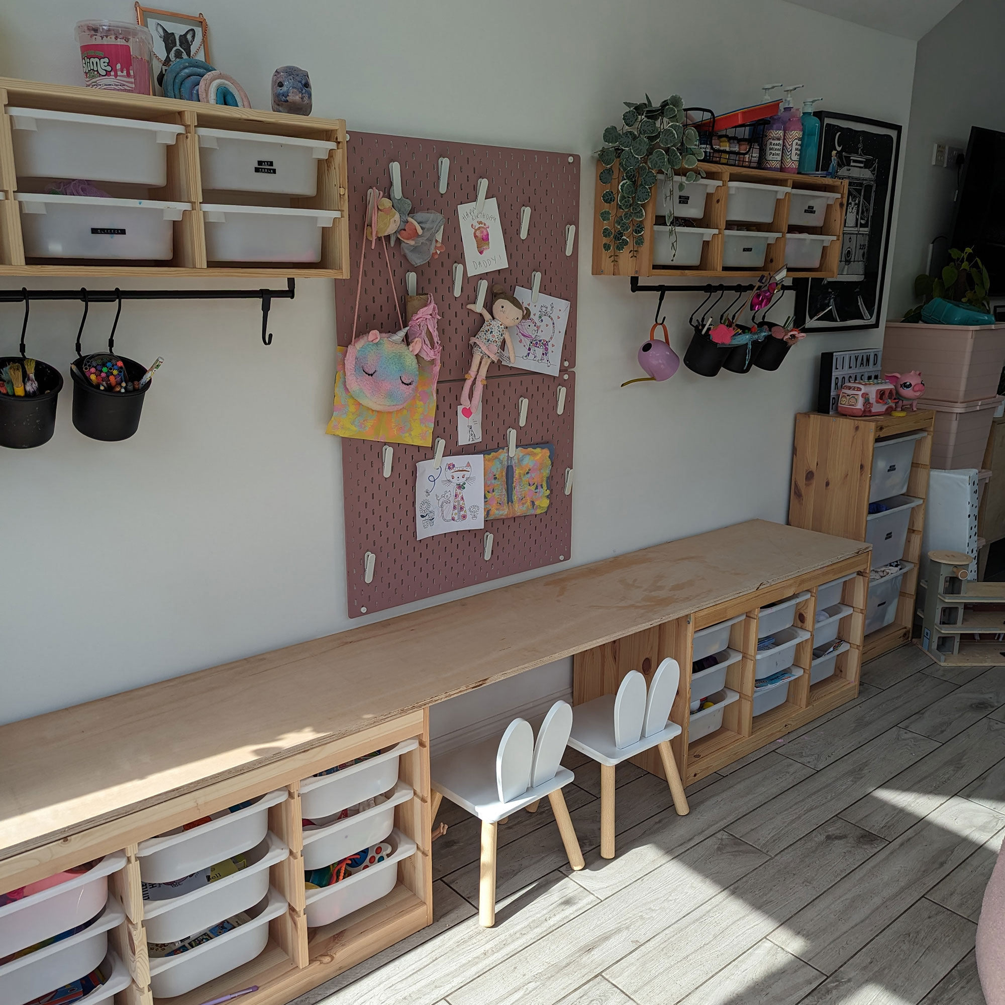 Kids room with long wooden desk, trays for toys and craft and pinboard