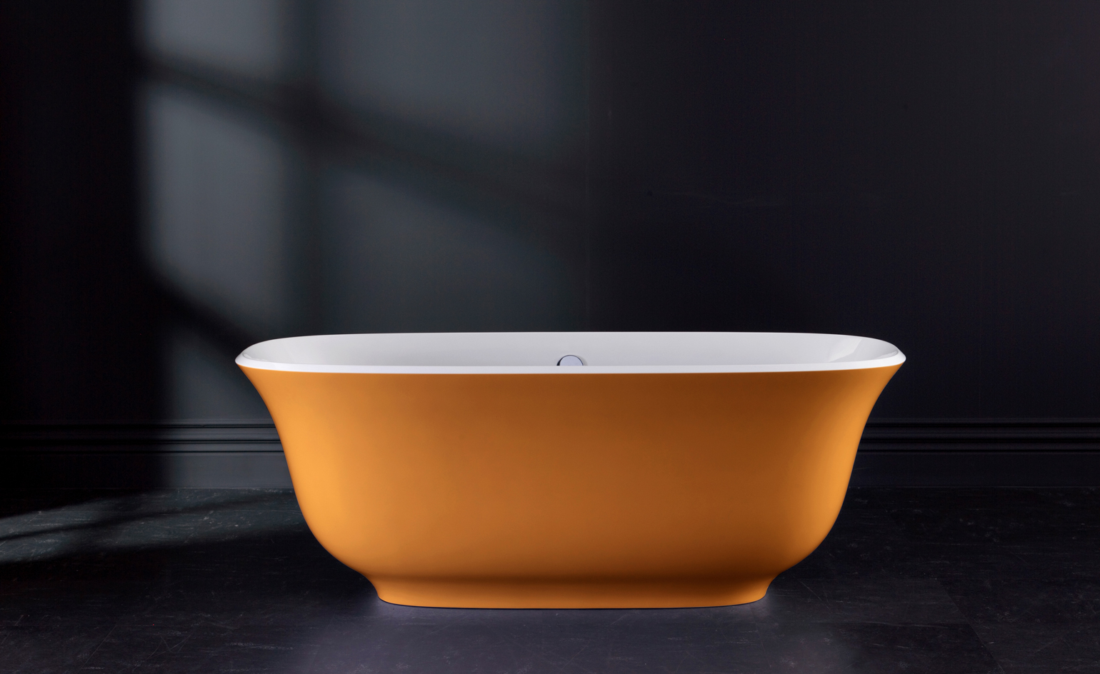 Orange ‘Amiata’ volcanic limestone bathtub by House of Rohl against a dark background