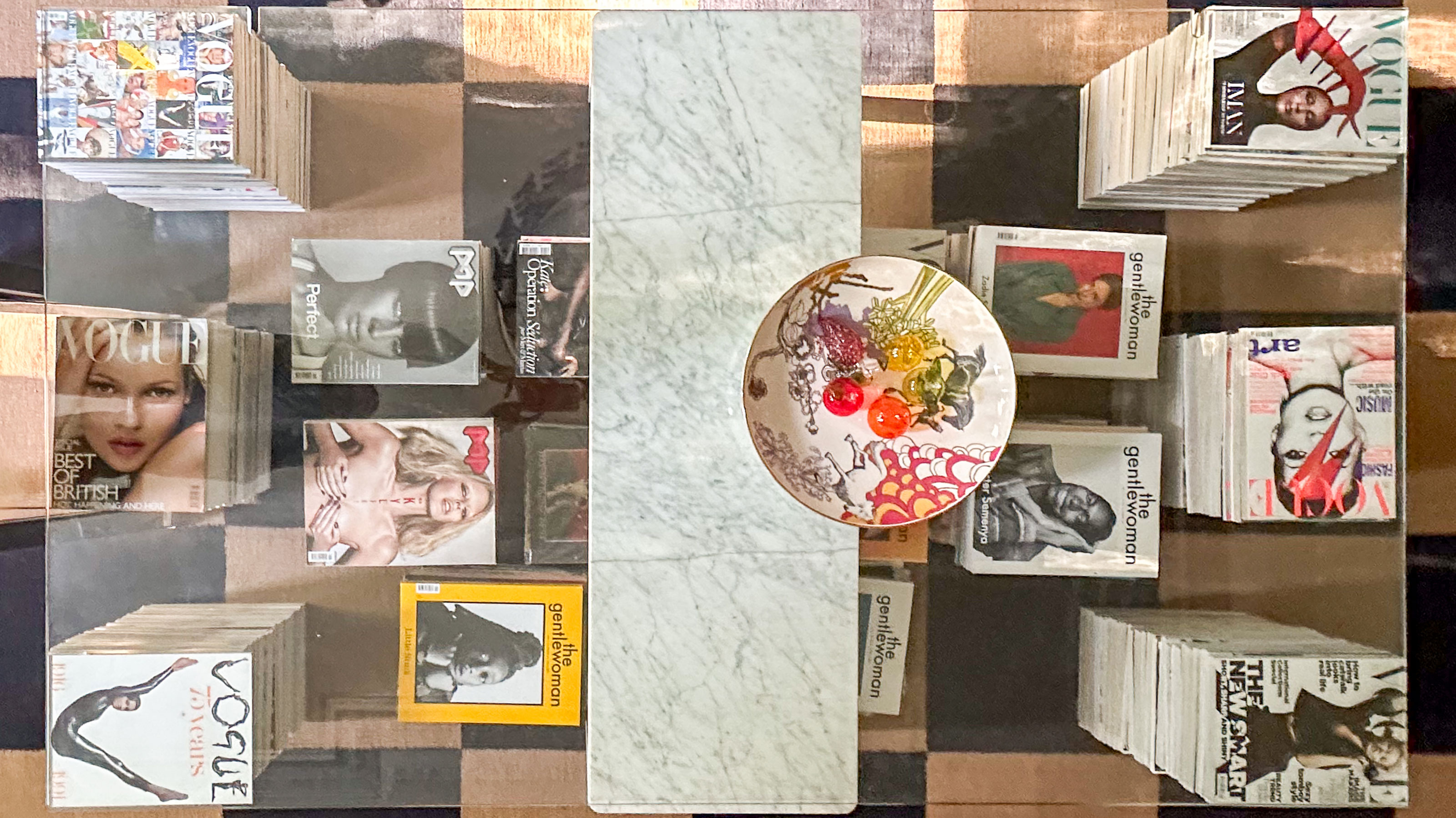 Glass topped coffee table propped up with marble and stacks of magazines
