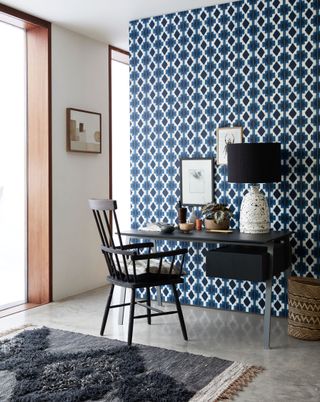 Geometric blue and white printed wallpaper in a home office with black table and chair.