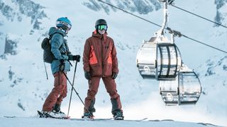 Two skiers chat on the slopes of Chamonix with gondola cabins in the background