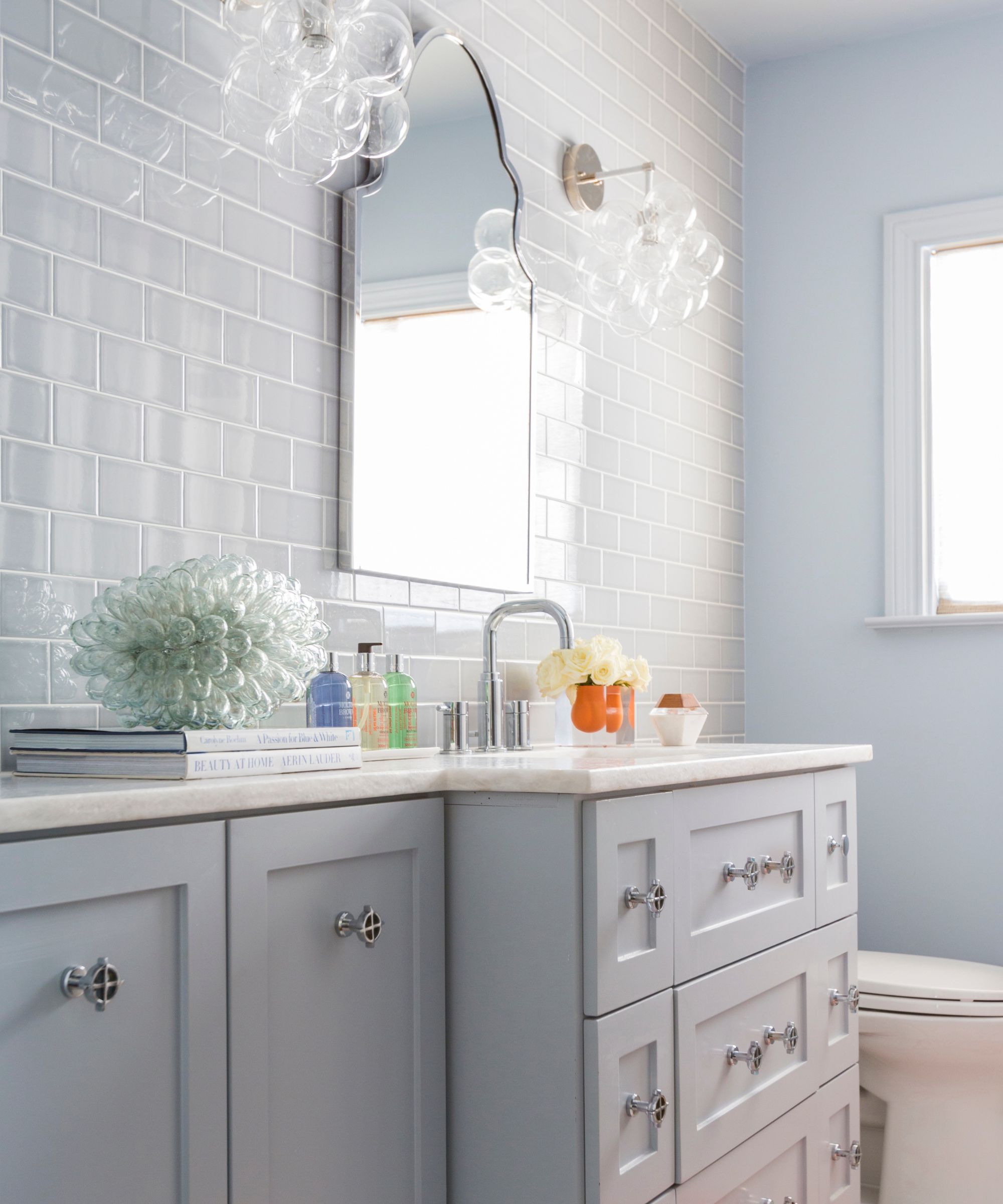 A light and airy bathroom with pale blue walls and vanity, white counters, and a gray-blue tiled wall.