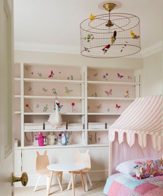 child's bedroom with white built in storage shelves, metal birdcage pendant light with birds on and pink wallpaper in shelving