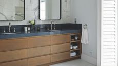 a bathroom with a wood vanity with storage for bathroom trinkets, a dark countertop and double sinks with mirrors 