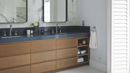 a bathroom with a wood vanity with storage for bathroom trinkets, a dark countertop and double sinks with mirrors 