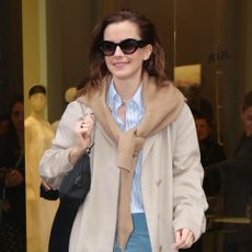 Emma Watson styles a trench coat and jumper over her shoulders.