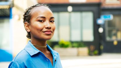 A millennial woman in a blue shirt smiles at the camera.