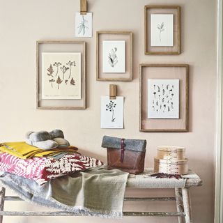 Woven bench covered in blankets, slippers, and boxes with a gallery wall of flower frames above it